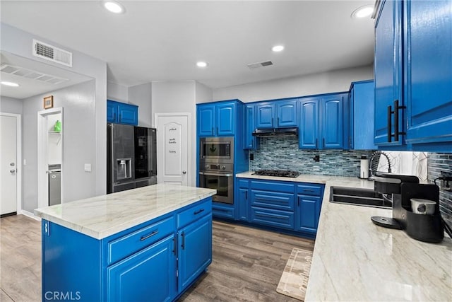 kitchen featuring stainless steel appliances, wood finished floors, visible vents, blue cabinetry, and light stone countertops