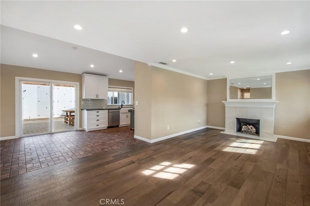 unfurnished living room featuring crown molding, dark hardwood / wood-style flooring, a tiled fireplace, and sink