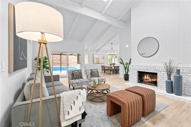 living room with beam ceiling, a fireplace, wood finished floors, a notable chandelier, and high vaulted ceiling