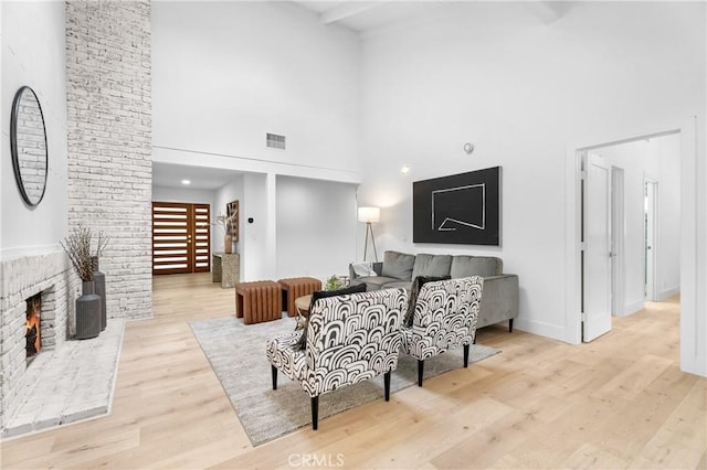 living room featuring a towering ceiling, a brick fireplace, and light wood-type flooring