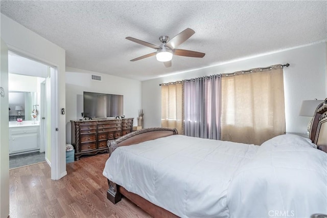 bedroom with wood-type flooring, ceiling fan, a textured ceiling, and ensuite bath