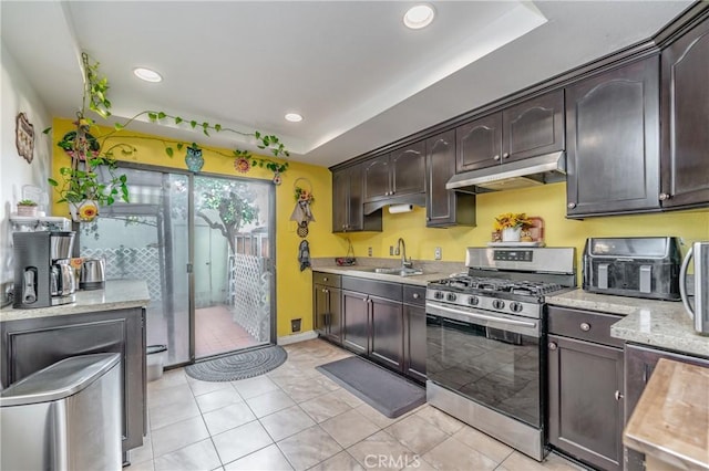 kitchen with stainless steel gas range oven, sink, dark brown cabinetry, and a tray ceiling