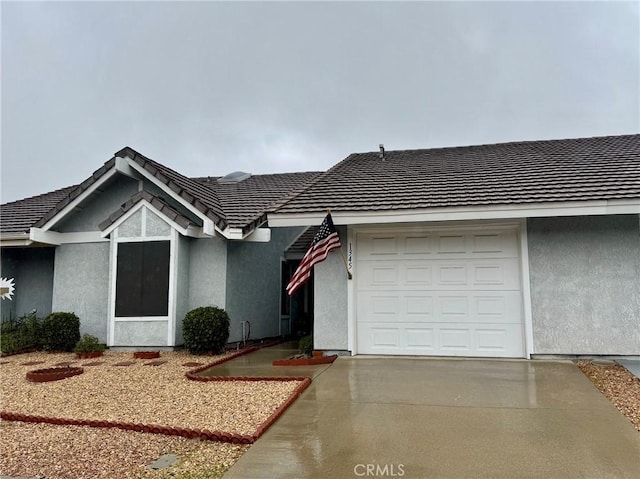 ranch-style home with concrete driveway, a tiled roof, an attached garage, and stucco siding