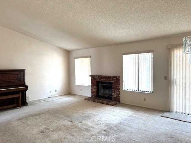 unfurnished living room featuring lofted ceiling, a textured ceiling, carpet, and a brick fireplace