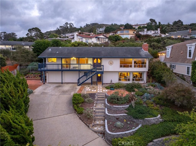 view of front of home with driveway, a balcony, a chimney, an attached garage, and stairs