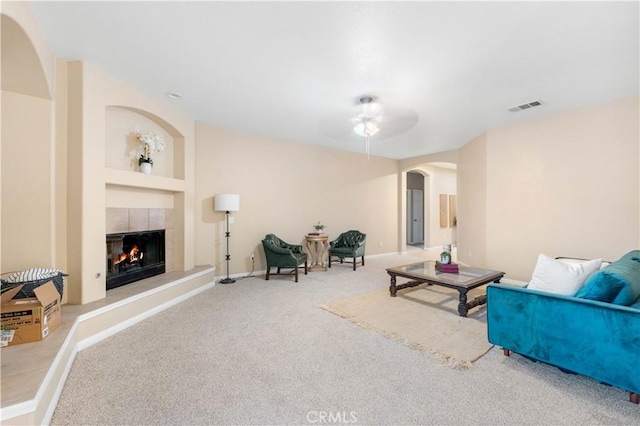 living room featuring a tiled fireplace, carpet flooring, ceiling fan, and built in shelves