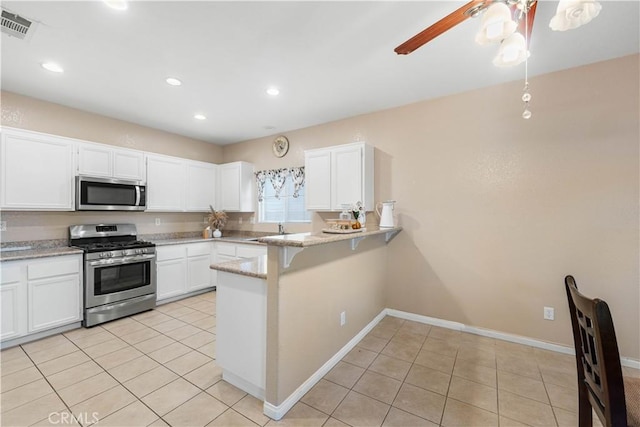 kitchen with light tile patterned flooring, white cabinets, light stone counters, kitchen peninsula, and stainless steel appliances