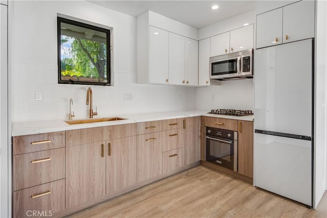 kitchen with sink, tasteful backsplash, stainless steel appliances, light hardwood / wood-style floors, and white cabinets