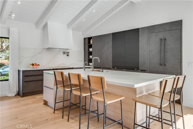 kitchen with lofted ceiling with beams, a breakfast bar, a spacious island, and premium range hood