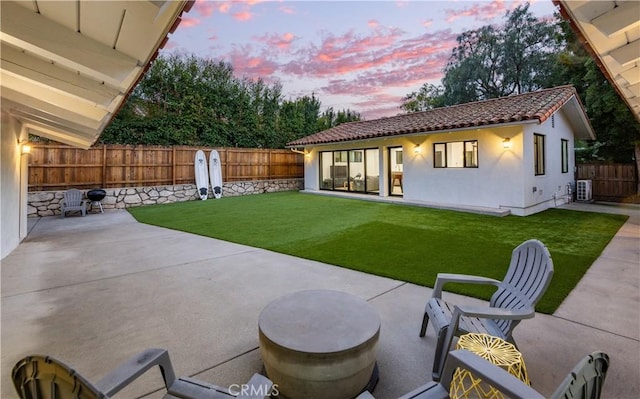 back house at dusk with a yard, central AC unit, and a patio