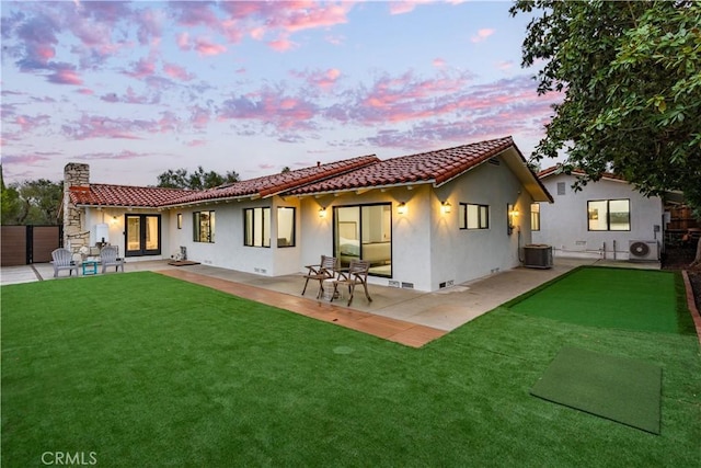 back house at dusk with a yard, ac unit, a patio, and central air condition unit