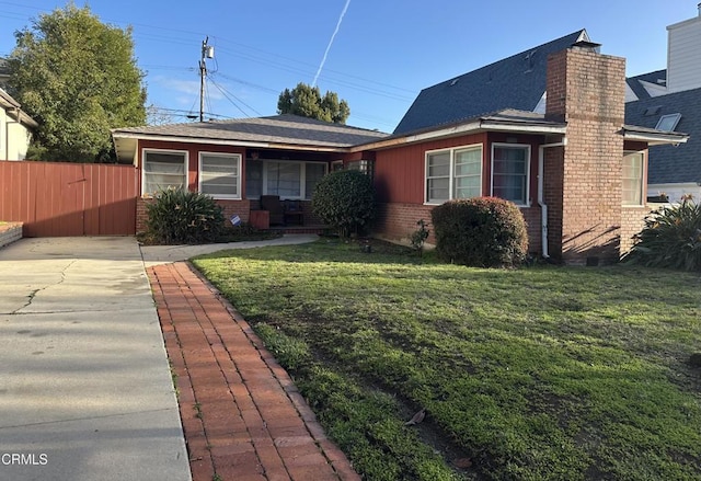 view of front of house with a chimney, fence, a front lawn, and brick siding