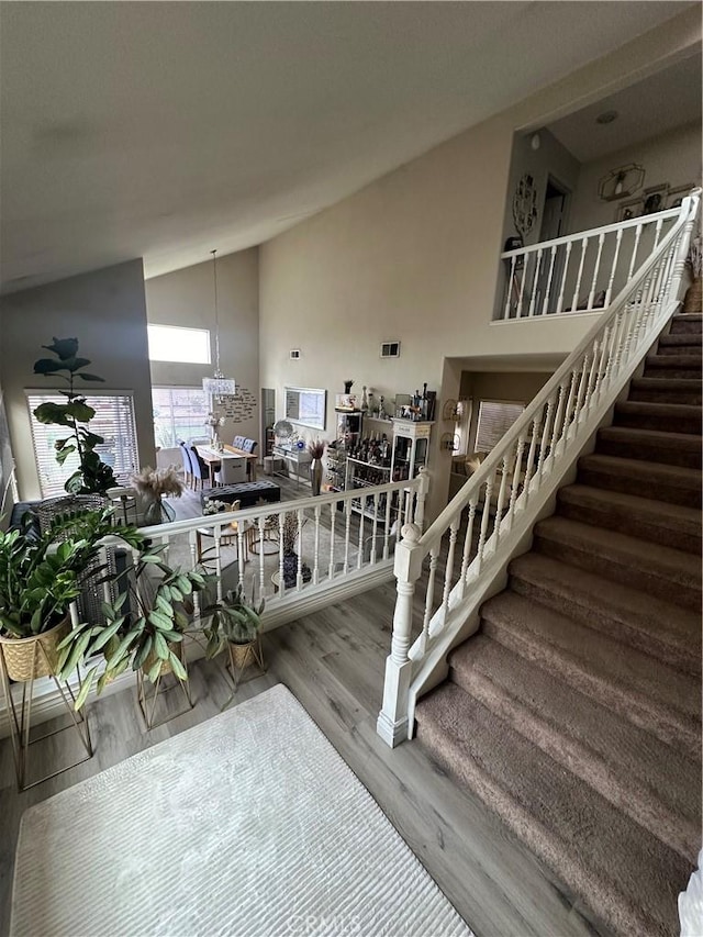 staircase with wood-type flooring and high vaulted ceiling