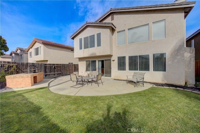 rear view of property with stucco siding, a patio area, fence, and a lawn