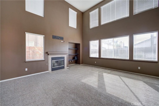 unfurnished living room featuring a tile fireplace, a towering ceiling, and light carpet