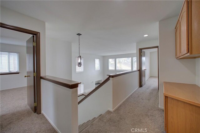 corridor featuring light colored carpet, plenty of natural light, and an upstairs landing