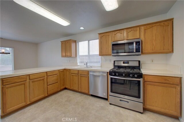 kitchen featuring a peninsula, recessed lighting, tile countertops, a sink, and stainless steel appliances
