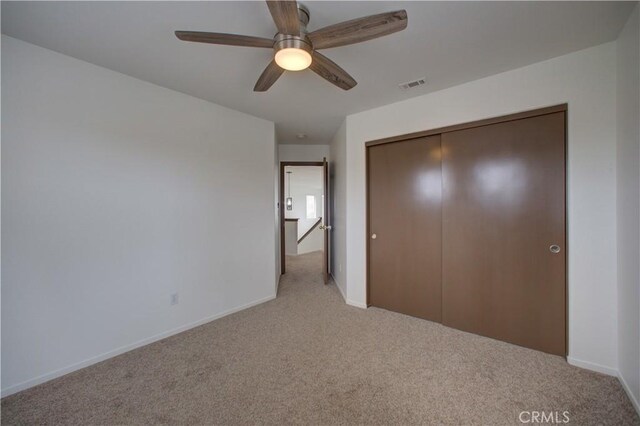 unfurnished bedroom featuring light colored carpet, a ceiling fan, baseboards, visible vents, and a closet