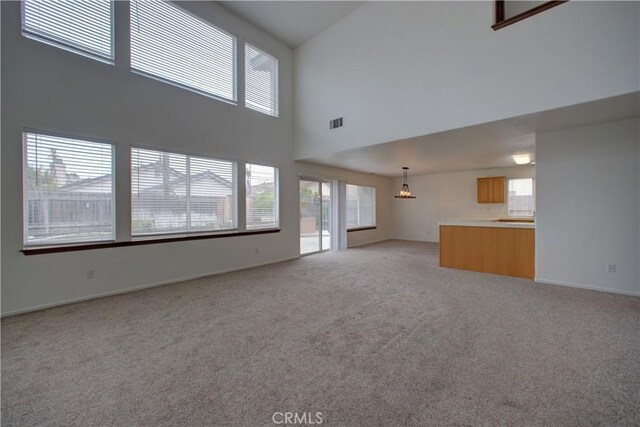 unfurnished living room featuring light carpet, a sink, baseboards, a towering ceiling, and visible vents