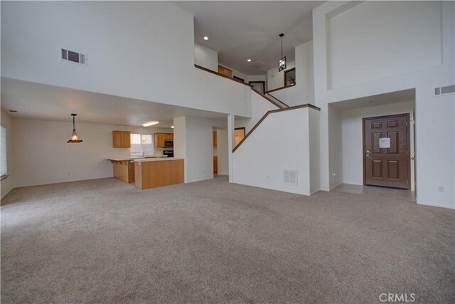 unfurnished living room with visible vents, light carpet, and a towering ceiling
