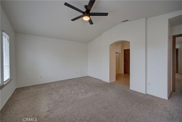 empty room with light colored carpet, arched walkways, a ceiling fan, lofted ceiling, and visible vents