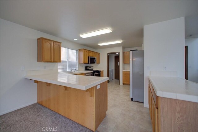 kitchen featuring a peninsula, a breakfast bar, baseboards, tile counters, and appliances with stainless steel finishes