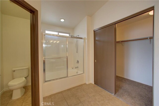 bathroom with toilet, a spacious closet, combined bath / shower with glass door, and tile patterned flooring
