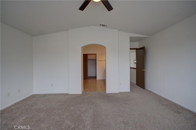 carpeted spare room with ceiling fan, visible vents, arched walkways, vaulted ceiling, and baseboards