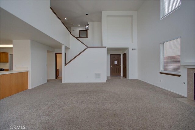 unfurnished living room featuring visible vents, a towering ceiling, stairway, baseboards, and light carpet