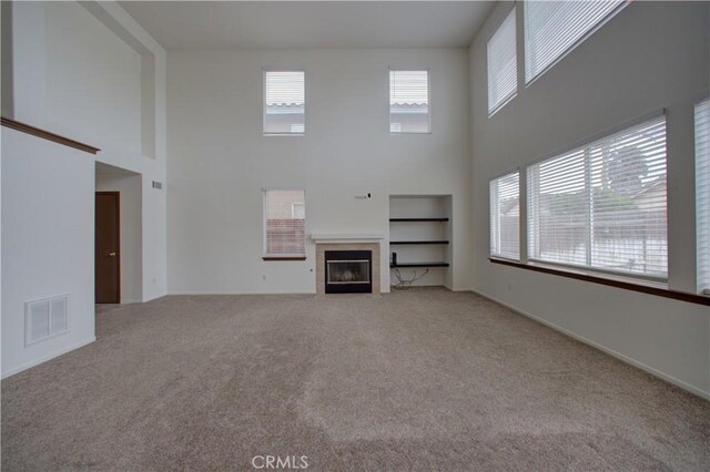 unfurnished living room featuring visible vents, carpet, a towering ceiling, and a fireplace