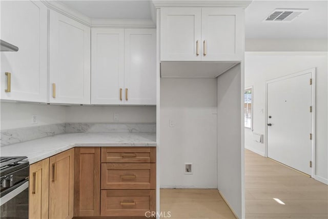 kitchen featuring light stone counters, gas stove, white cabinets, and light wood-type flooring