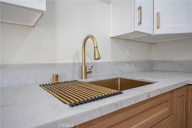 interior details featuring white cabinetry, sink, and light stone counters