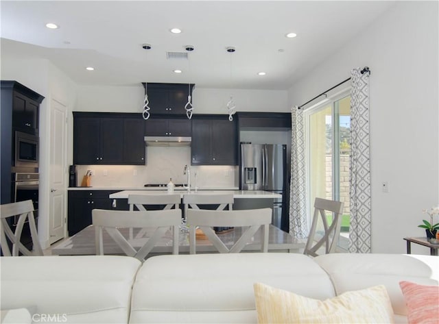 kitchen featuring a center island with sink, visible vents, appliances with stainless steel finishes, dark cabinetry, and under cabinet range hood