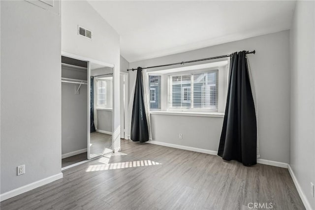 unfurnished bedroom featuring wood-type flooring, lofted ceiling, and a closet