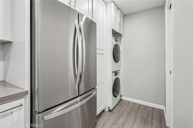 kitchen with stacked washer / drying machine, stainless steel fridge, white cabinets, and light wood-type flooring