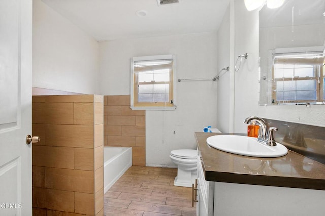 bathroom featuring vanity, toilet, tile walls, and a washtub