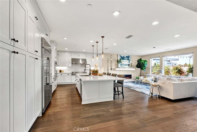 kitchen with a breakfast bar area, decorative light fixtures, dark hardwood / wood-style flooring, a kitchen island with sink, and white cabinets