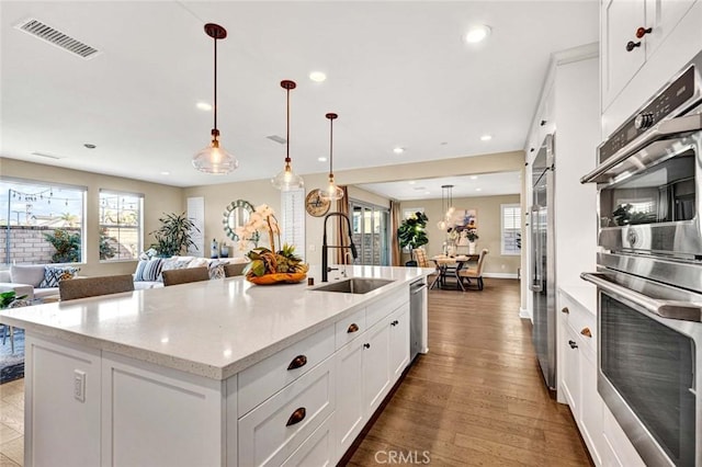 kitchen featuring hanging light fixtures, white cabinetry, sink, and a kitchen island with sink