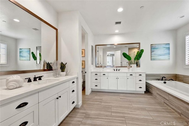 bathroom with vanity, toilet, and tiled bath