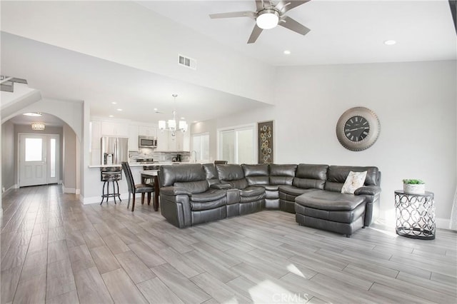 living room featuring vaulted ceiling, ceiling fan with notable chandelier, and light hardwood / wood-style floors