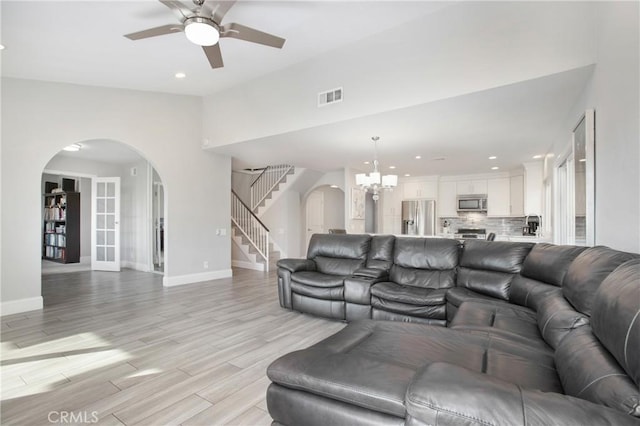 living room featuring vaulted ceiling, ceiling fan with notable chandelier, and light hardwood / wood-style flooring