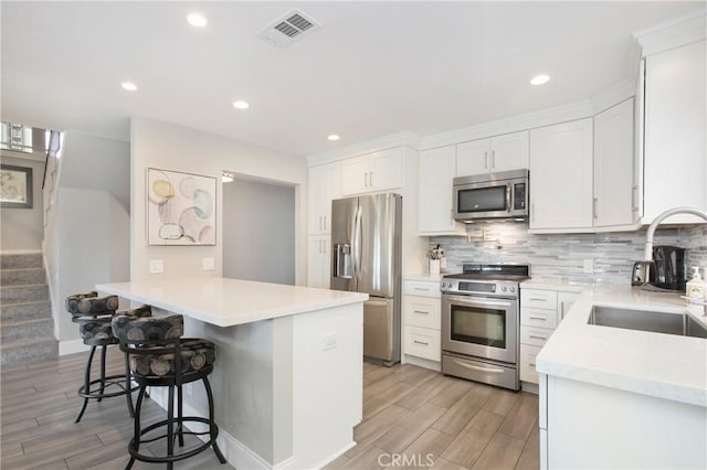 kitchen featuring sink, a breakfast bar, white cabinetry, stainless steel appliances, and kitchen peninsula