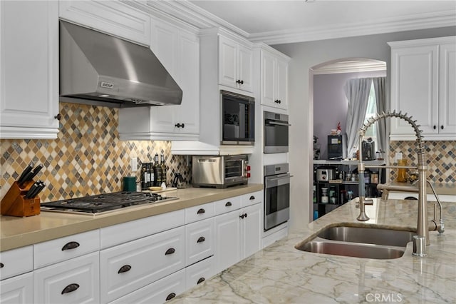 kitchen with white cabinets, stainless steel appliances, sink, and wall chimney range hood