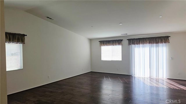 spare room with dark wood-style floors, visible vents, and vaulted ceiling