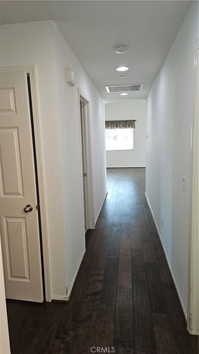 hall with dark wood-style floors, visible vents, and baseboards