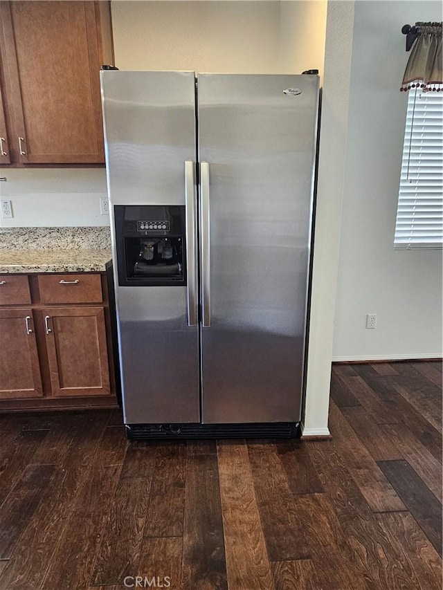 kitchen featuring brown cabinetry, stainless steel refrigerator with ice dispenser, dark wood finished floors, and light stone countertops