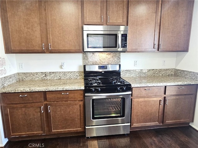 kitchen featuring appliances with stainless steel finishes, dark wood-type flooring, light stone counters, and brown cabinets