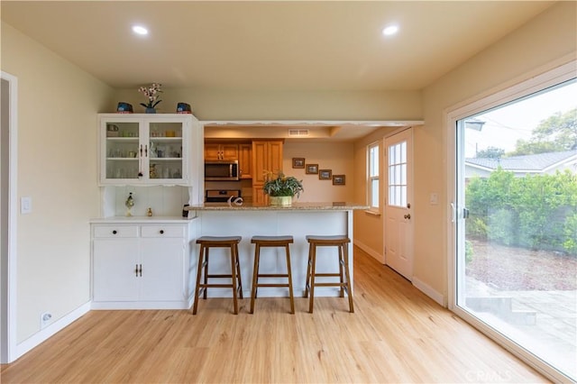 kitchen featuring light hardwood / wood-style flooring, stainless steel appliances, a kitchen bar, and kitchen peninsula