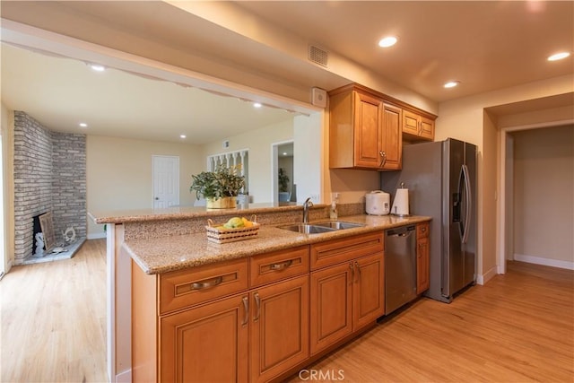 kitchen with a brick fireplace, light hardwood / wood-style floors, sink, light stone counters, and appliances with stainless steel finishes