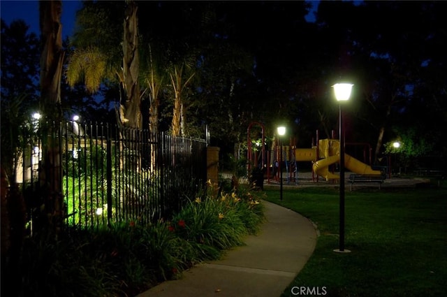 playground at night featuring fence, playground community, and a yard